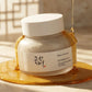 Angle : 3/4 face  Beauty of Joseon Ground Rice and Honey Glow Mask jar partially surrounded by flowing golden honey, realistic honey drips, warm sunlight, luxury Korean skincare campaign, photorealistic cosmetic photography, premium beauty advertising, creamy texture visible through frosted glass, elegant shadows, ultra detailed. (gemini-3.1-flash-image-preview)