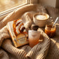 Un visuel lifestyle chaleureux à 1200x1200px. Le parfum et sa boîte d'image_9539c2.jpg sont installés sur un plaid en maille épaisse de couleur beige. À côté, une tasse de macchiato fumante et un petit pot de caramel. Une lumière douce de fin d'après-midi traverse une fenêtre invisible, projetant des ombres douces et créant une atmosphère réconfortante. (gemini-3-pro-image-preview)