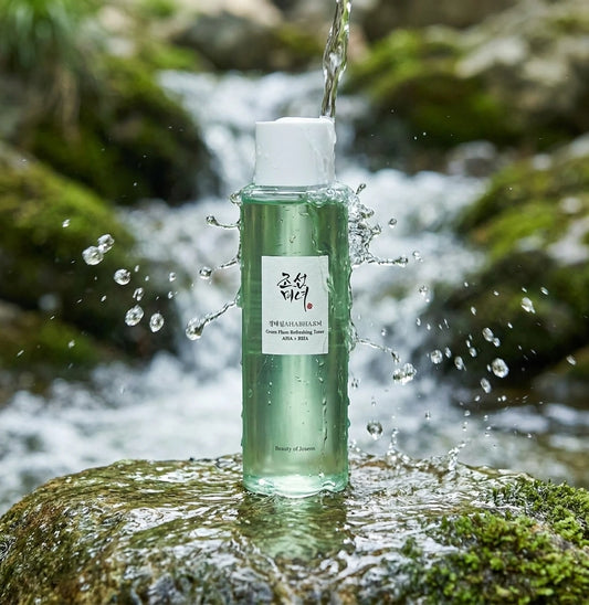 Angle légèrement en contre-plongée  Beauty of Joseon Green Plum Refreshing Toner placed on wet stone beneath a gentle waterfall, crystal clear water splashing naturally around the bottle, realistic droplets frozen in motion, premium skincare campaign, refreshing hydration concept, ultra realistic lighting, luxury cosmetic photography. (gemini-3-pro-image-preview)