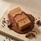 Angle : Vue plongeante à 30°  Le parfum Arabiyat Prestige Toffee Ganache entouré d'une ganache au chocolat brillante qui s'étale naturellement sur une surface en pierre beige. Quelques éclats de cacao et copeaux de chocolat décorent la scène. Photographie publicitaire réaliste. (gemini-3-pro-image-preview)