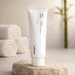 Premium spa product photography. A "Celimax Noni Energy Repair Cream" jar placed on a rough, textured raw stone block. In the blurred background, rolled white cotton towels and a subtle green bamboo stalk. Warm, relaxing diffused lighting, high-end wellness aesthetic, photorealistic --ar 1:1 (gpt-image-1.5)