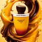 Une composition publicitaire dynamique au format carré de 1200x1200px. Au centre, le flacon de parfum "Arabiyat Sugar - Mango Affogato" de image_952660.jpg est mis en valeur à la verticale. En arrière-plan immédiat, un tourbillon artistique et fluide mêle un coulis de mangue jaune orangé et un filet de café espresso crémeux et sombre, rappelant le concept de l'affogato. L'éclairage est studio et vif, faisant briller le bouchon sombre et rendant l'inscription "Mango Affogato" parfaitement nette. (gpt-image-2